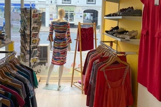 View through a shop with rails of clothes each side and back of mannequin in window display
