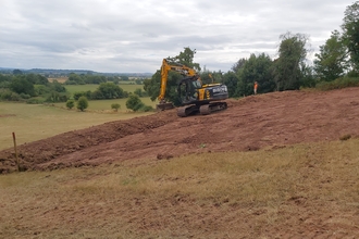 Small yellow digger moving earth on sloping field