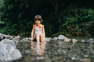 Young girl sat on pebbles in a river