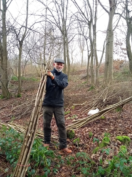 Man holding long sticks stood in a woodland in winter