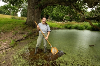 Woman stood in edge of pond with a dipping net, looking forwards