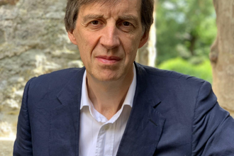 Head & shoulders portrait of a man in a blue formal jacket and white open necked shirt