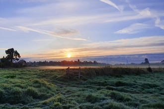 Sun rising over a meadow; blue sky streaked with cloud