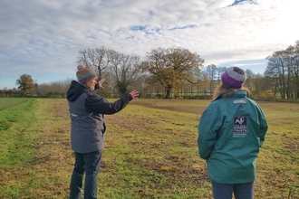 Two women in coats and hats in a field with trees in the background