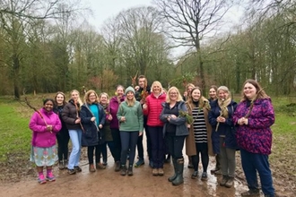 Group of people smiling at the camera holding twigs outdoors with woodland in background