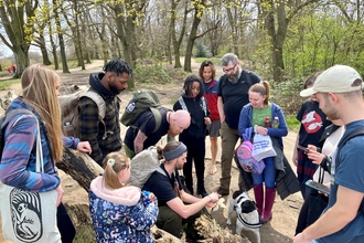 A group of people surrounding their walk leader looking at a woodland plant that he is showing them