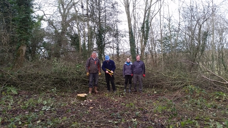 Four people stood in a woodland clearing facing the camera, winter