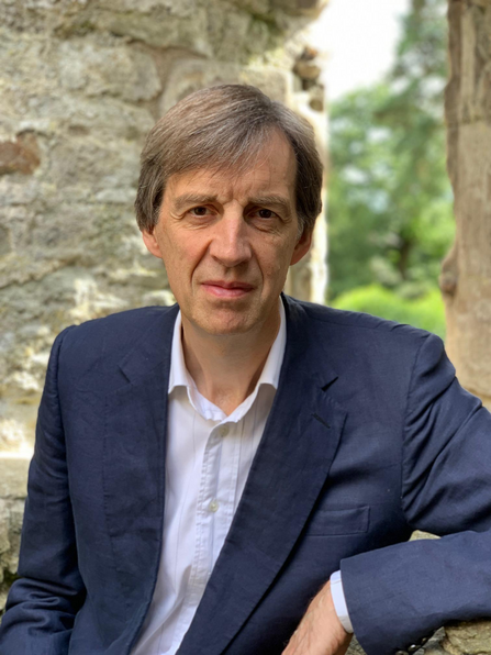 Head & shoulders portrait of a man in a blue formal jacket and white open necked shirt