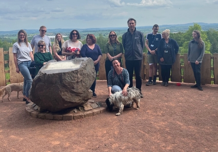 Group of people stood by large stone with view across landscape in background