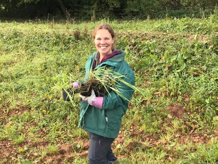 Woman in green coat smiling at camera holding plants