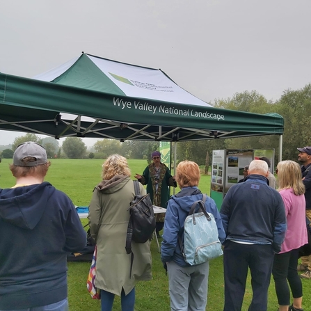 Small group of people stood around a green gazebo in a green field