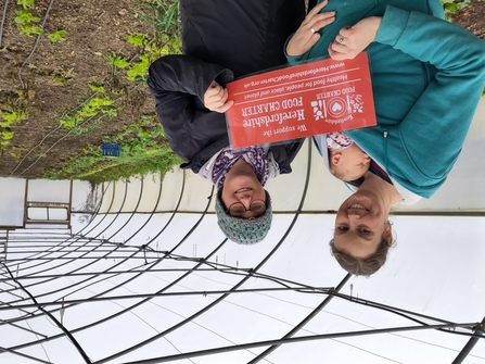 Two women and a baby in a polytunnel holding up a Food Charter sign