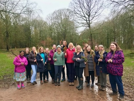 Group of people smiling at the camera holding twigs outdoors with woodland in background