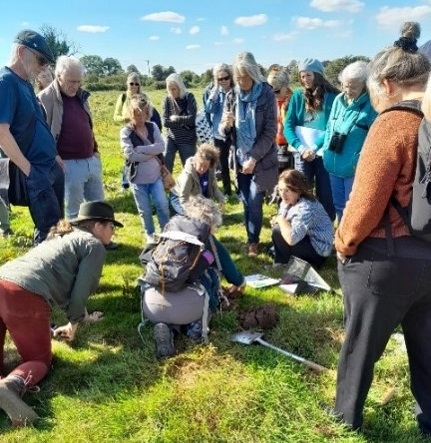 Group of people stood outdoors with those in the centre kneeling looking at the grass