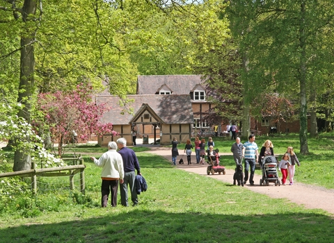 Families walking on tree-lined path with timber-framed buildings in background