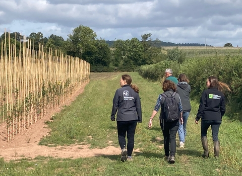 five people walking beside an arable field in the countryside